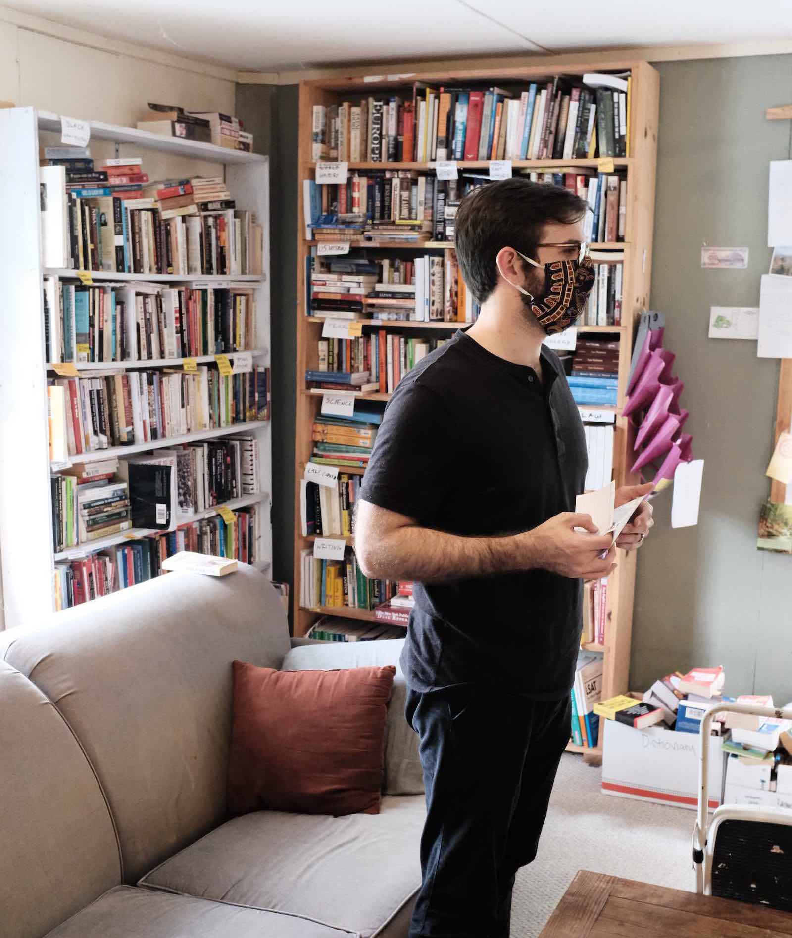 A volunteer with a mask standing in front of a bookshelf